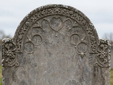 Close-up of a weathered nineteenth-century headstone carving, soft overcast light highlighting the deep slate gray stone textures