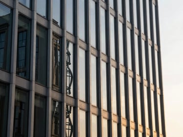 Architectural detail of a glass and steel corporate facade reflecting warm sunset light, sharp lines, editorial composition.