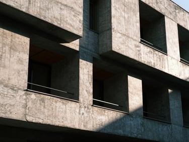Close-up of a cured concrete architectural model facade, harsh late-afternoon sunlight casting deep shadows across brutalist window openings, high contrast