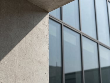 Extreme close-up of raw textured concrete meeting a clean glass facade, sharp diagonal shadows under hard sunlight