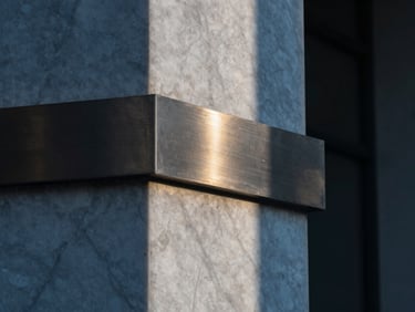 Extreme macro detail of a brushed steel and white marble architectural column, sharp geometric shadows, cool blue tones with a sliver of golden light
