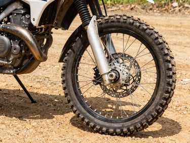 Close-up of a dusty Yamaha motorcycle tire and engine suspension on a rugged dirt road in Guaviare, high contrast.