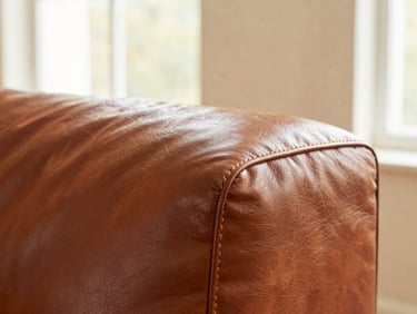 Macro shot of immaculate double-stitching on a rich cognac leather sofa, warm natural window light, shallow depth of field
