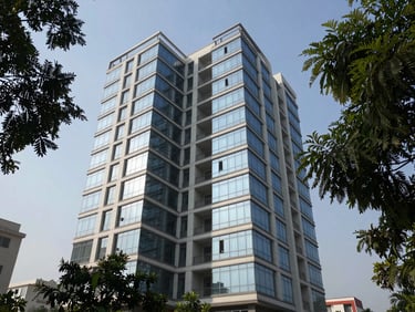 Mid-rise residential building facade in Aerocity Mohali photographed in natural daylight, clean glass-and-concrete finish, mature trees framing the frame edges