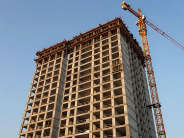 Ground-level view of a premium pre-launch residential tower under construction in Mohali, concrete frame visible against clear blue sky, cranes in background, golden afternoon light on facade