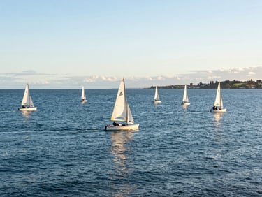 Wide environmental shot of Christchurch Harbour at golden hour with multiple small sailing dinghies on calm water, low horizon, bright coastal daylight.