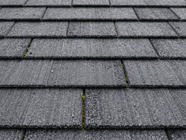 Identical close-up of pristine, clean asphalt shingles, completely free of black streaks and moss, showing original slate gray texture.