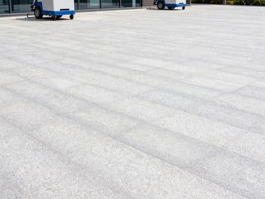 Wide shot of a clean commercial paved area, industrial cleaning equipment subtly in the background, bright overcast daylight, clean stone textures, crisp architectural photography