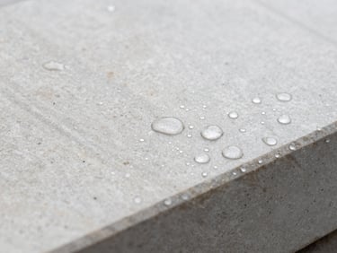 Macro shot of water beading on a freshly impregnated stone surface, showing water droplets forming perfect spheres, bright overcast daylight, clean stone textures, crisp architectural photography