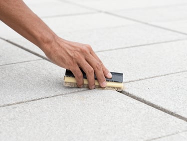 Close-up of hands carefully sweeping jointing sand into paving gaps, bright overcast daylight, clean stone textures, crisp architectural photography, sharp details
