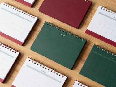 Overhead flat-lay of curated corporate calendars and wooden promotional gadgets on a light oak table, soft Scandinavian daylight, matte finish