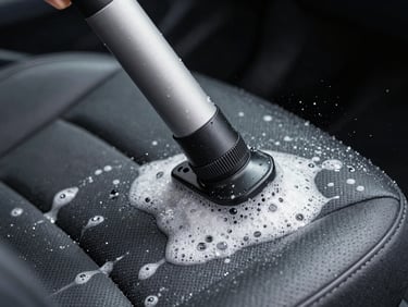 Extreme close-up of a commercial hot-water extraction wand pressed into a car seat, moisture and foam visible on dark fabric, cool studio-quality daylight, sharp focus on the tool-to-surface contact point
