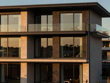 Architectural close-up of a modern luxury house facade with large glass windows and minimalist design, golden hour sunlight, rich deep tones.