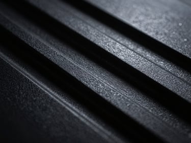 Macro shot of a dark textured polymer surface with precise geometric ridges, dramatic side lighting, deep shadows