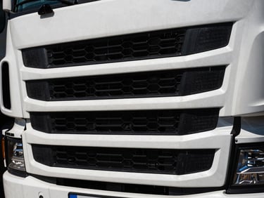 Close-up of a modern semi-truck grille, sharp focus, high contrast, deep shadows, cinematic photography.