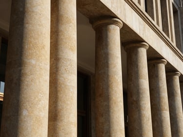 Macro architectural photograph of curved hotel lobby columns wrapped in warm sand travertine flexible stone, low-angle natural light, deep shadows