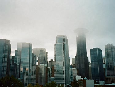 Wide environmental shot of the Seattle skyline shrouded in thick morning mist, modern glass skyscrapers reflecting cool blue-hour light, 35mm film.