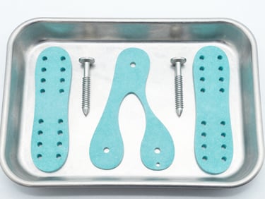 Flat-lay of sterile orthopedic fixation plates and locking screws on a clean surgical tray, bright clinical lighting, sharp focus
