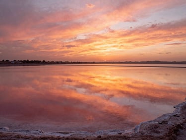 Cinematic shot of the salt flats of San Pedro at sunset, vibrant pink and orange reflections on the water surface.