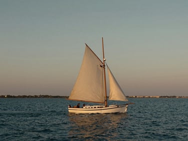 Cinematic wide-angle shot of a classic sailing boat gliding through the calm waters of the Mar Menor lagoon, soft dusk lighting