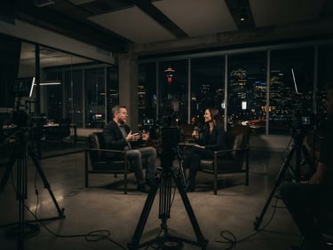 Wide cinematic environmental shot of a professional multi-camera interview setup in a modern downtown Calgary office, dramatic low-key lighting, deep shadows, 35mm anamorphic lens.