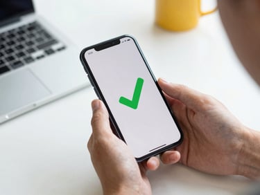 Hands holding a modern smartphone with a green success checkmark on screen, daylight, crisp workspace details