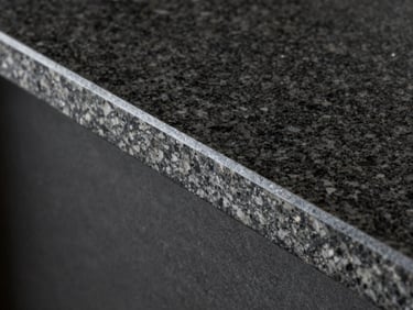 Architectural detail of a finished stone edge profile on a dark granite countertop, clean lines, blueprint style lighting.