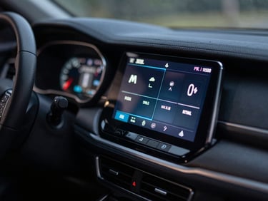 Tight macro shot of a modern car dashboard infotainment screen glowing in a low-light cabin interior, displaying channel information and digital text on the display.