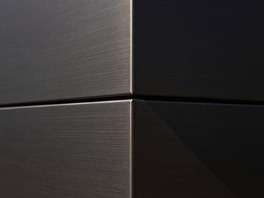 Tight abstract macro shot of brushed dark metal panels meeting at a precise geometric seam, architectural shadow casting a sharp diagonal line, minimalist composition.