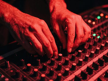 Intimate close-up of hands adjusting dials on a vintage mixing console under deep red neon light, high contrast, 35mm film grain