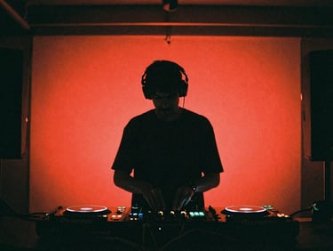 Moody low-key shot of a DJ in a dark cable-filled booth, silhouette against red neon lights, raw basement atmosphere