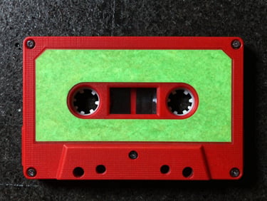 Gritty flash photo of a cassette tape with handwritten neon green label, dark concrete background