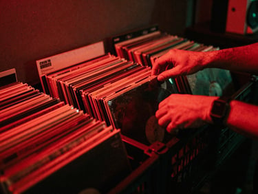 Hands of a DJ sorting through a crate of vinyl records in a dark, red-lit studio, high contrast shadows