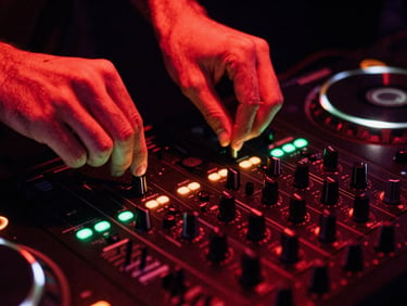 Hands of a DJ on a mixing console with glowing green LED meters, dark studio