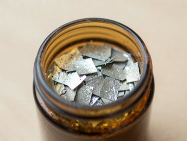 Close-up of magnesium flakes in a small amber glass jar on a light wood surface, soft diffused daylight, shallow depth of field, 35mm