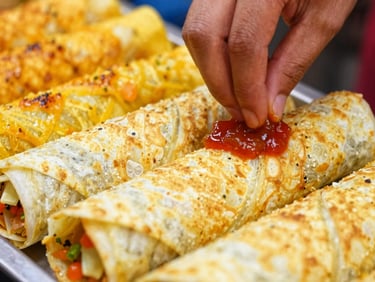 Close-up of a paneer kati roll being assembled, hands adding chutney, vibrant market colors.