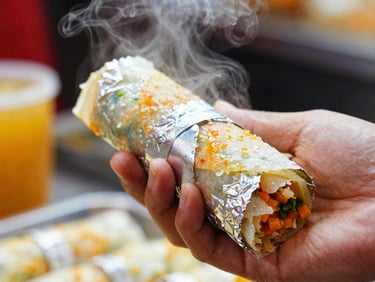 Close-up of a hand quickly wrapping a foil kati roll, steam rising, harsh market lighting, focus on motion