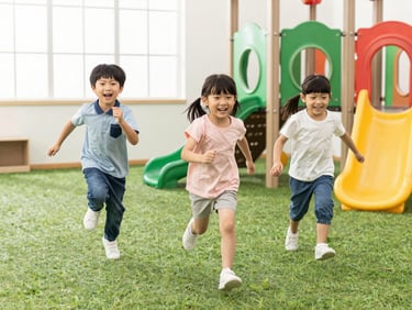 Happy young children running on a safe grassy playground with soft play equipment