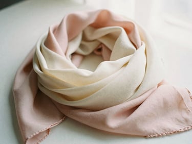 Softly folded pastel pink and cream scarves layered together under diffused window light, 35mm