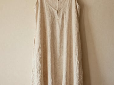 Editorial shot of a flowing beige linen dress hanging against a warm plaster wall, soft natural light, 35mm