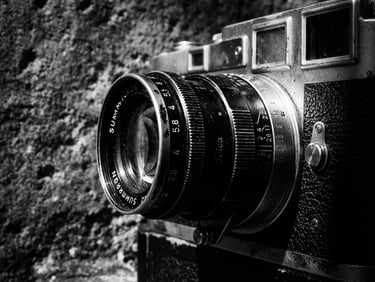 Gritty black and white close-up of a vintage 35mm film camera lens, harsh chiaroscuro lighting, concrete texture background