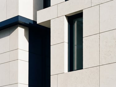 Minimalist architectural crop of a modern stone facade, clean geometric lines, soft morning window light, deep navy shadows, off-white textures, 35mm lens.