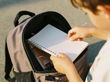 Close-up shot of a child's hands opening a new backpack filled with notebooks, soft daylight