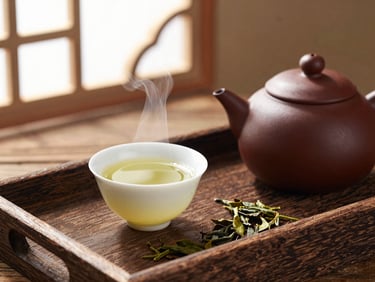 Steaming ceramic teapot beside a delicate cup of green tea, loose tea leaves scattered on a rustic wooden tray, 35mm