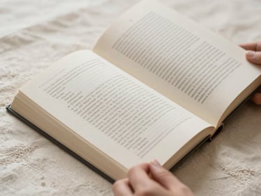 Single essay book lying open on a cream linen surface, hands just visible at the lower edge turning a page, soft diffused daylight from the left, close-up on paper texture and typeset columns