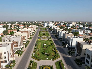 Wide-angle drone shot of Bahria Town Islamabad, manicured green spaces, wide paved roads, contemporary villas under clear blue sky
