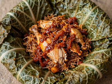 Overhead shot of Nasi Bungkus Ayam Pop, pale tender chicken, savory red sauce, crispy cabbage leaves.