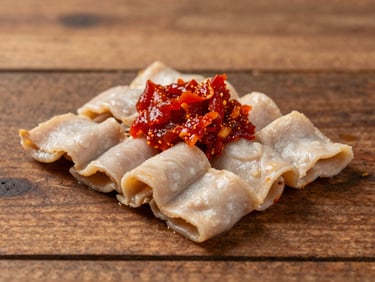 Tight shot of pale, tender ayam pop served with vibrant red sambal petai on the side, warm rustic wood background.