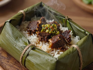 Overhead shot of Nasi Bungkus Rendang package, opened to reveal dark beef, cassava leaves, green sambal, and steaming rice.
