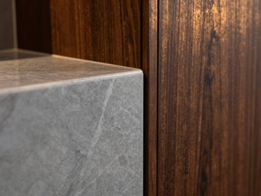 Macro close-up of a flawless seam between polished gray marble alternative and dark walnut wood paneling, warm architectural lighting, sharp focus on premium textures